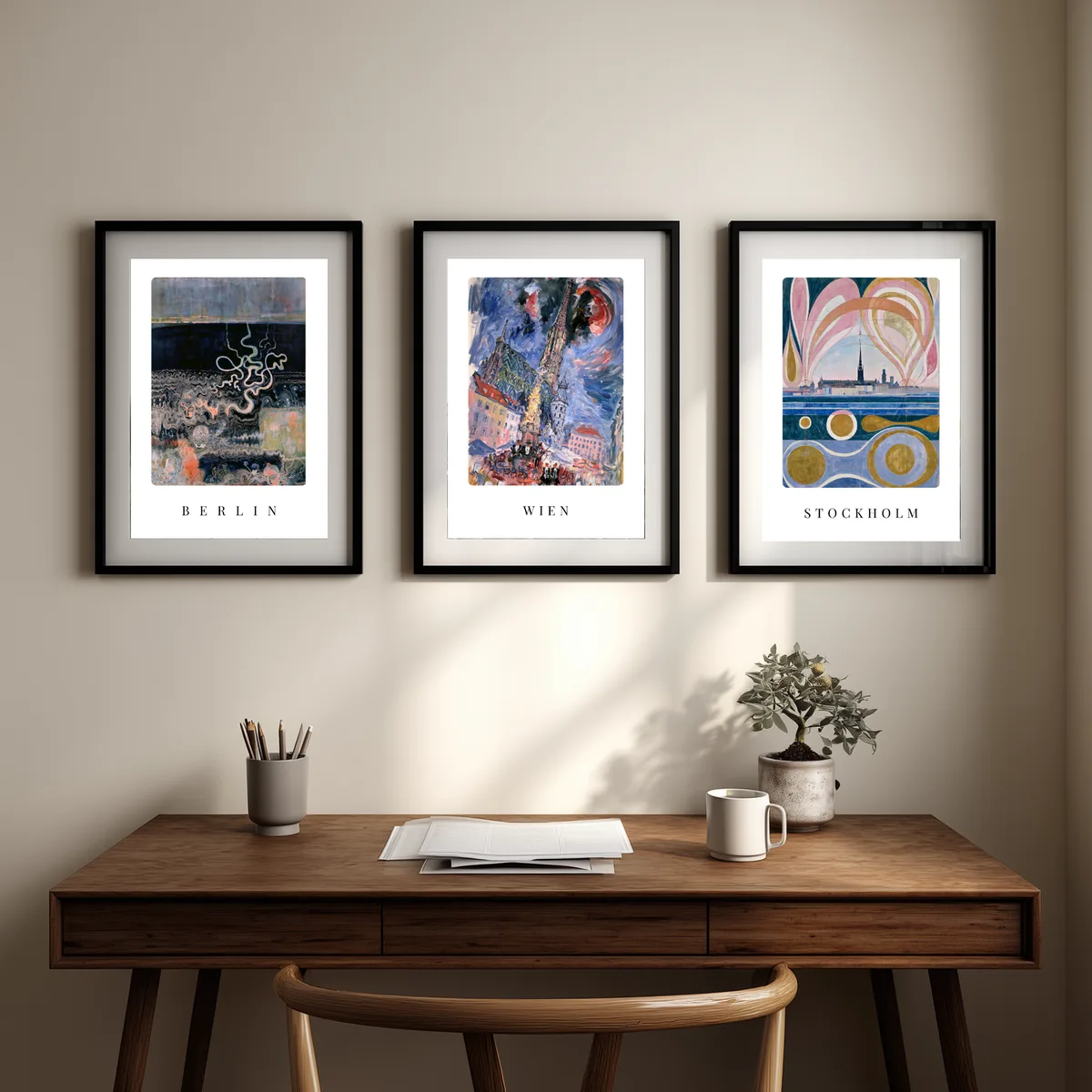 Die drei Poster Berlin, Wien und Stockholm nebeneinander über einem Schreibtisch